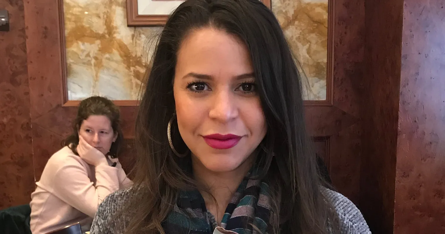 Arelis Caban-Oberst smiling at a cafe table, working through her weekly content on a coffee break.